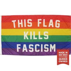 May include: A rectangular rainbow flag featuring horizontal stripes of red, orange, yellow, green, blue, and violet. The white text THIS FLAG KILLS FASCISM is printed across the center. A small red tag in the corner reads MADE IN SAN DIEGO QUEER OWNED.