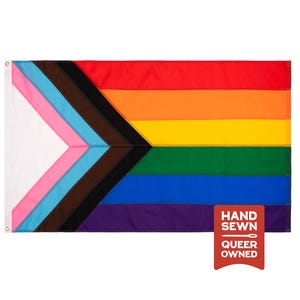 May include: A rectangular progress pride flag featuring horizontal stripes of red, orange, yellow, green, blue, and violet, with a chevron on the left containing white, pink, light blue, brown, and black stripes. A red tag reads HAND SEWN QUEER OWNED.