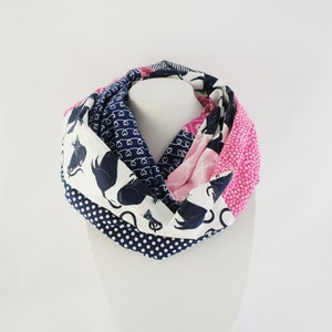 May include: A white, pink and navy blue infinity scarf with a black cat print. The scarf is made of cotton fabric and is soft and comfortable to wear.