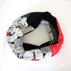 May include: A black, white and red infinity scarf with a pattern of sheep and balls of yarn. The scarf is made of fabric and has a soft, comfortable feel.