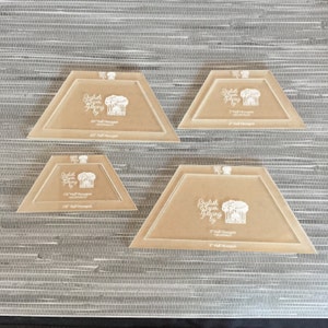 Może przedstawiać: Cztery przezroczyste szablony akrylowe do English Paper Piecing w różnych rozmiarach. Każdy szablon ma kształt połowy sześciokąta z zaokrąglonymi rogami i nadrukowanym wzorem. Rozmiary: 3,8 cm, 5,1 cm, 6,4 cm i 7,6 cm. Szablony ułożone są na teksturowanej, szarej powierzchni.