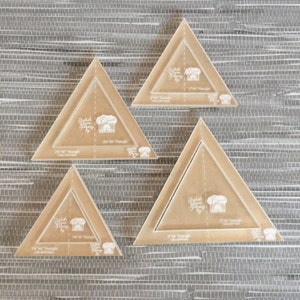 May include: Four clear acrylic quilting rulers in the shape of triangles. The rulers are labeled with their size in inches: 1 1/2", 2 1/2", 3", and 4".