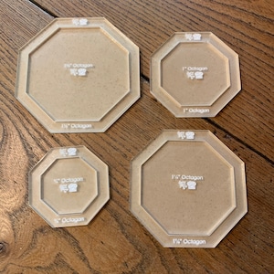 May include: Four clear plastic octagon-shaped templates for quilting or crafts. The templates are labelled with the size of the octagon in inches: 1/2", 3/4", 1", and 1 1/2".