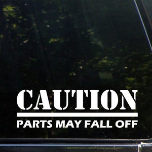 Könnte beinhalten: Weißer Vinyl-Aufkleber mit dem Text "CAUTION PARTS MAY FALL OFF" auf schwarzem Hintergrund.