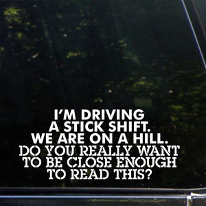 May include: A white vinyl sticker with the text "I'M DRIVING A STICK SHIFT. WE ARE ON A HILL. DO YOU REALLY WANT TO BE CLOSE ENOUGH TO READ THIS?"