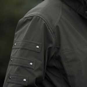 Close-up of olive green GORE-TEX winter jacket sleeve with metal rivets and detailed stitching.