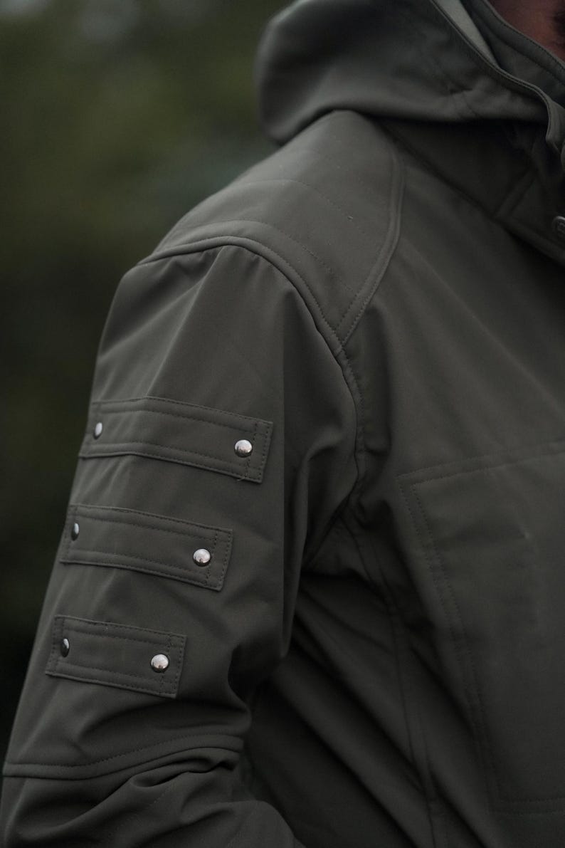 Close-up of olive green GORE-TEX winter jacket sleeve with metal rivets and detailed stitching.