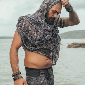May include: A patterned scarf with a snake skin design is draped over the head and shoulders. The person is wearing patterned shorts with a black waistband. The person is also wearing bracelets and an arm band.