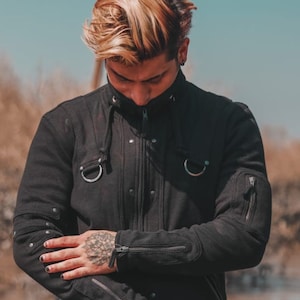 May include: A person wearing a black hooded jacket with zipped pockets and silver hardware. The jacket has a distressed look and the person has a tattoo on their left hand.
