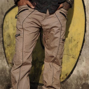 May include: A pair of beige cargo trousers with black trim and multiple pockets. The trousers have a geometric pattern.