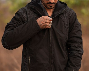 May include: A black hooded jacket featuring a full-length front zipper, long sleeves with zippered cuffs, and side panels adorned with a geometric pattern. The garment includes a hood and two vertical zippered pockets on the front torso area.