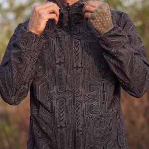 Peut inclure: Une veste noire à capuche avec un motif géométrique. La veste a une fermeture éclair et une capuche à cordon.
