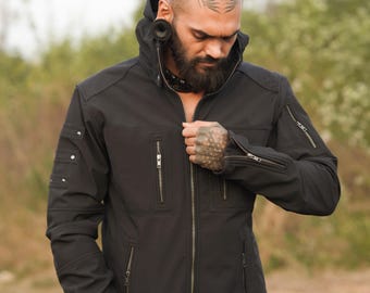 May include: A black softshell jacket with a zipper closure, multiple pockets, and a high collar. The jacket has a modern, utilitarian design.