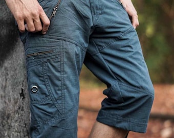 May include: Blue-grey cargo shorts featuring multiple pockets with metallic zippers, a reinforced panel on the thigh, a silver-toned metal grommet detail on the side pocket, and adjustable drawstring ties at the hem of each leg opening.