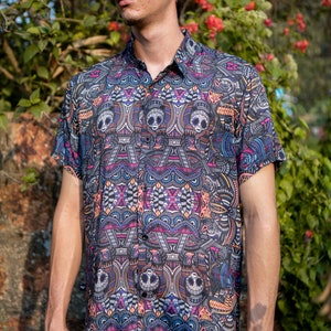 May include: A short-sleeved button-down shirt with a colourful, geometric pattern featuring skulls and other abstract designs. The shirt is black with pink, blue, yellow, and white accents.