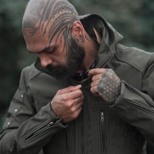 Man wearing windproof olive green soft shell winter jacket zipping up front closure.