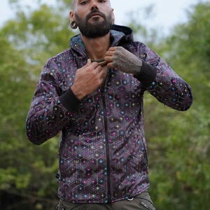 Könnte beinhalten: Eine Kapuzenjacke mit Reißverschluss und einem geometrischen Sechseckmuster in Dunkelviolett und Schwarz, verziert mit kleinen, leuchtenden, bunten Akzenten. Die Jacke verfügt über einen durchgehenden Frontreißverschluss, eine Kapuze und schwarze Rippbündchen.