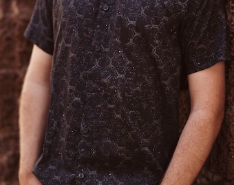 May include: A black short-sleeved button-down shirt with a geometric pattern. The shirt has a subtle sheen and a relaxed fit.