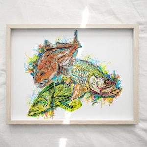 May include: Framed art print featuring three colorful fish illustrations. The artwork showcases a red, green, and teal fish with vibrant splashes of yellow, blue, and orange. The print is set in a light wood frame.