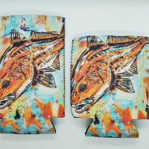 May include: Two redfish are depicted on a pair of colorful can coolers. The fish are drawn in a stylized, almost abstract style, with a splash of color behind them. The can coolers are made of neoprene and have a zippered closure.