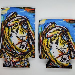 May include: Two colorful can coolers with a painted image of a face. The face is yellow, white, and black with blue and red accents. The background is blue with white and yellow brushstrokes.
