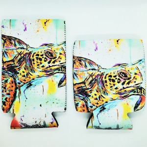 May include: Two colorful can coolers with a sea turtle design. The turtles are painted in shades of yellow, orange, green, and blue on a white background with splashes of color.