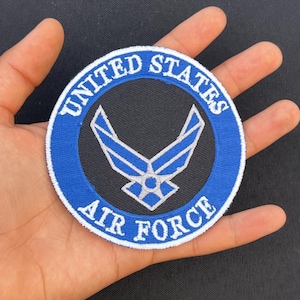 Peut inclure: Un écusson brodé bleu et blanc avec les mots "United States Air Force" en cercle autour d'un emblème de l'Air Force argenté.