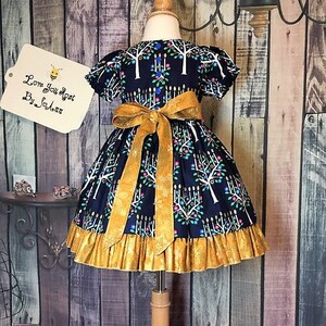 Peut inclure: Robe bleu marine avec un n&oelig;ud et une bordure dor&eacute;s. La robe pr&eacute;sente un motif d'arbres et de bougies blancs. Le texte "Love You Most By SoAnn" est sur une &eacute;tiquette. La robe est pr&eacute;sent&eacute;e sur un mannequin.
