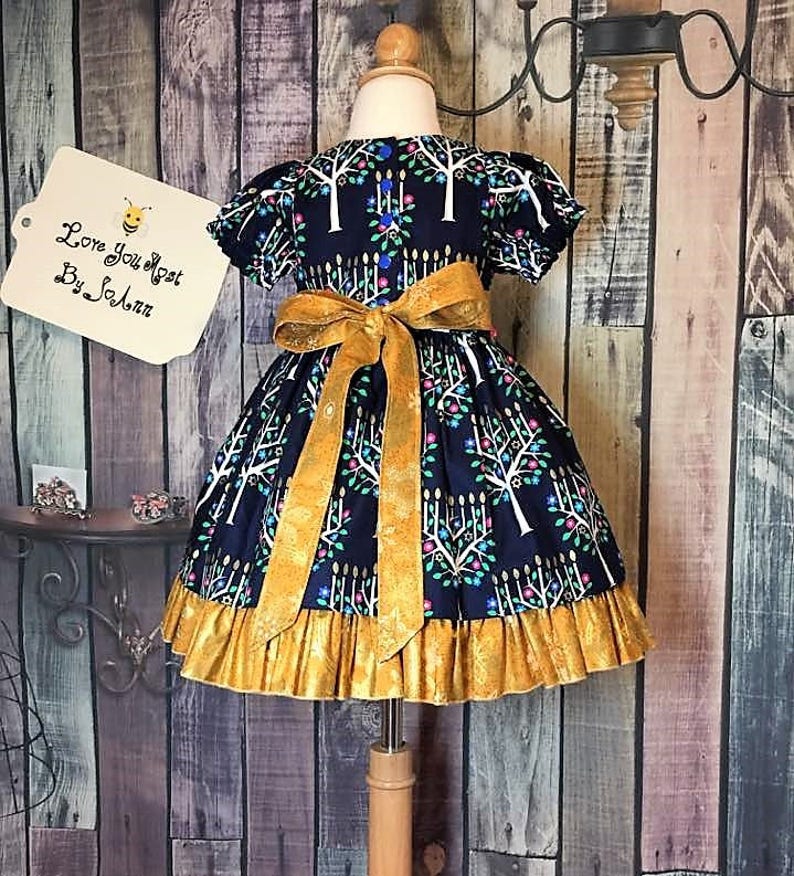 Peut inclure: Robe bleu marine avec un n&oelig;ud et une bordure dor&eacute;s. La robe pr&eacute;sente un motif d'arbres et de bougies blancs. Le texte "Love You Most By SoAnn" est sur une &eacute;tiquette. La robe est pr&eacute;sent&eacute;e sur un mannequin.