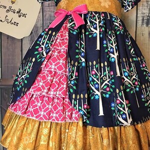 Peut inclure: Robe bleu marine avec un motif d'arbres et de fleurs, une ceinture dor&eacute;e et un n&oelig;ud rose. La robe a un panneau &agrave; motifs roses et blancs et un ourlet &agrave; volants dor&eacute;s. Robe pour enfant.