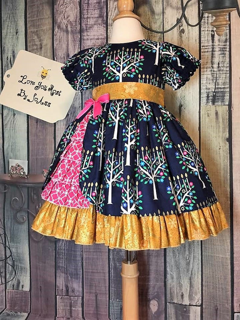 Peut inclure: Robe bleu marine avec un motif d'arbres blancs, une ceinture dor&eacute;e et un n&oelig;ud rose. La robe a un ourlet &agrave; volants et un panneau &agrave; motifs roses. L'&eacute;tiquette indique "Love You Most By SoAnn".