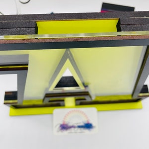 May include: A wooden letter "A" with a yellow background and black outline. The letter is layered with black and brown accents. The letter is standing on a yellow base.