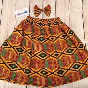 Könnte beinhalten: Ein gelber, roter, grüner und schwarzer gemusterter Rock mit einer passenden Schleife. Der Rock hat einen elastischen Bund und eine ausgestellte Silhouette.