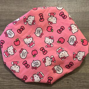 May include: Pink Hello Kitty shower cap with a repeating pattern of Hello Kitty characters, red bows, and apples. The text "Hello Kitty" appears in a speech bubble.