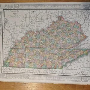 Può includere: Una mappa stampata vintage del Kentucky e del Tennessee con contee color pastello, linee di griglia nere e confini statali circostanti. La mappa include una scala, una legenda e il testo Kentucky and Tennessee, Atlas of the World.