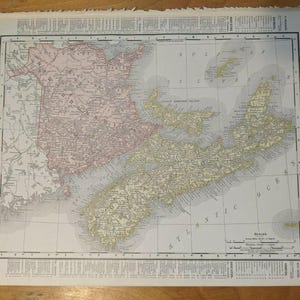 Op de afbeelding: Een vintage gedrukte kaart getiteld Atlas of the World met de Maritieme Provincies. De kaart toont New Brunswick in een lichtroze tint en Nova Scotia in lichtgeel, met zwarte tekstlabels voor steden, regio's en de Atlantische Oceaan.