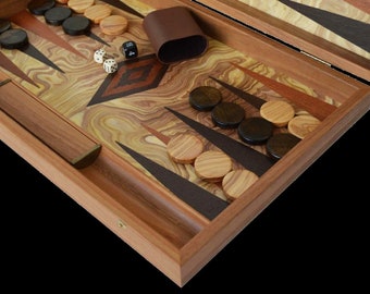May include: A wooden backgammon set with a light wood playing surface and dark wood accents. The set includes black and light-colored wooden game pieces, dice, and a brown leather dice cup. The game board is open and ready for play.
