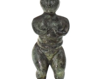 May include: A small, green bronze sculpture of a standing female figure. The figure has a rounded, stylized body and a simple, abstract face.