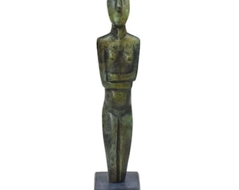 May include: A bronze sculpture of a standing figure with arms crossed. The figure has a simplified, stylized form and is mounted on a black base.