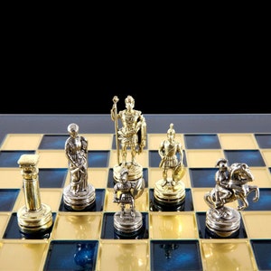 May include: A chess set with gold and silver pieces on a blue and gold chessboard. The pieces are in the shape of Roman soldiers and a column.