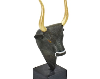 Pode incluir: Escultura de cabeça de touro preta com chifres dourados sobre uma base preta.