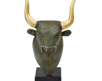 Pode incluir: Uma escultura de cabeça de touro de bronze com chifres dourados sobre uma base preta. Os olhos do touro são vermelhos.
