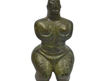 May include: A green bronze sculpture of a female figure with exaggerated features. The figure is standing with its arms crossed over its chest and has a pointed head.