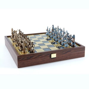 May include: A wooden chessboard with a brown finish and a gold trim. The chess pieces are made of metal and are in the shape of warriors. The pieces are arranged on the board in a starting position. The board is closed and has a latch.