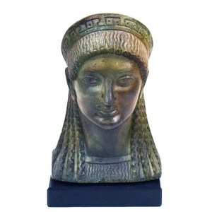 Può includere: Busto in bronzo di una donna con i capelli lunghi e una corona. Il busto è su una base nera.