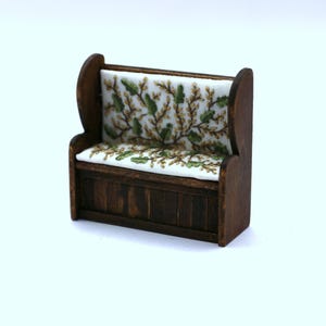 May include: Miniature wooden bench with a dark stain. The bench features a white cushion and backrest with a green and brown floral pattern. The bench is a decorative item.
