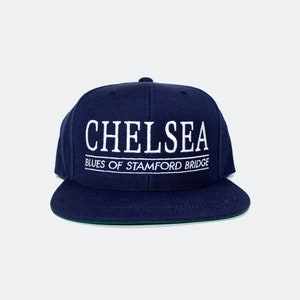 May include: A navy blue baseball cap with white embroidered text that reads "Chelsea Blues of Stamford Bridge".