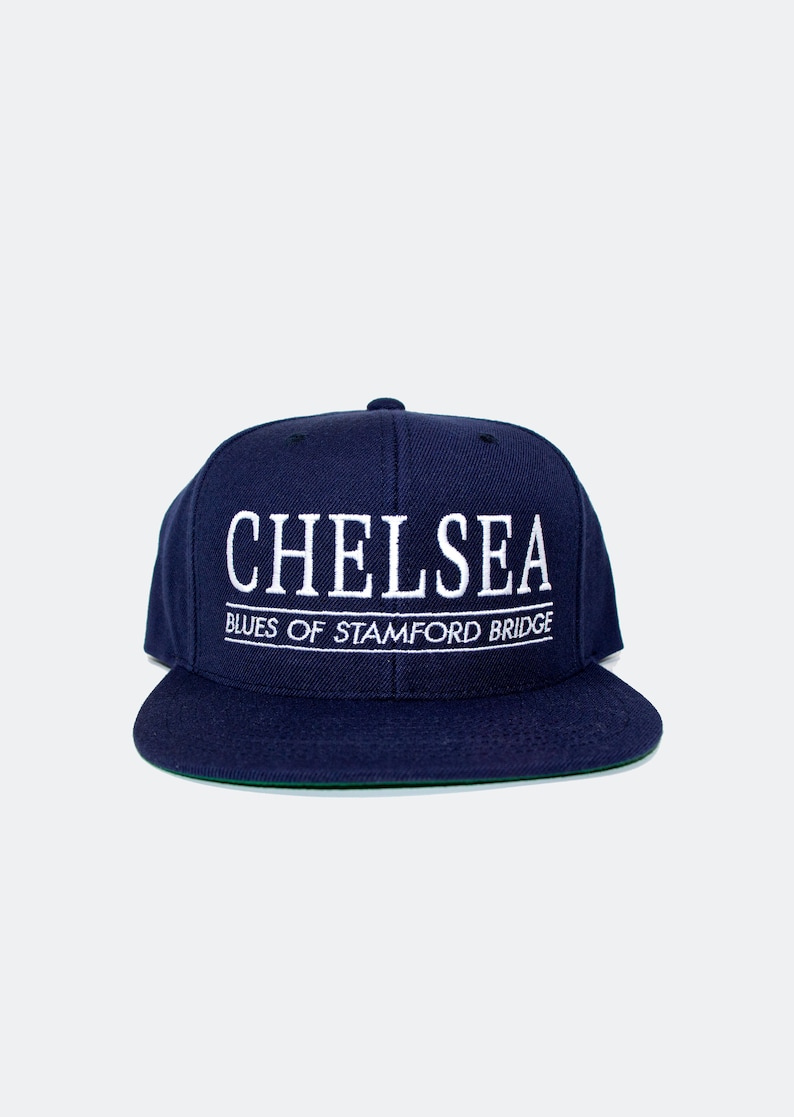 May include: A navy blue baseball cap with white embroidered text that reads "Chelsea Blues of Stamford Bridge".