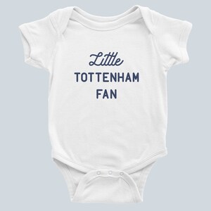May include: White baby onesie with short sleeves and navy blue text that reads "Little Tottenham Fan".