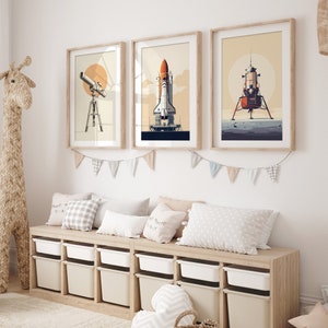 Pu&ograve; includere: Tre stampe artistiche incorniciate con illustrazioni a tema spaziale. Le stampe raffigurano un telescopio, uno space shuttle e un modulo lunare, il tutto in stile retr&ograve; con una calda tavolozza di colori. Le cornici sono in legno chiaro, e le opere d'arte sono esposte sopra una panca contenitore.